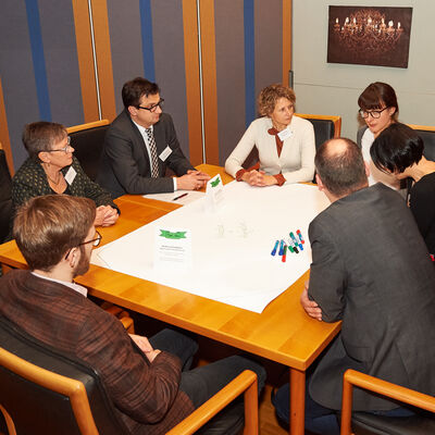 Bild vergrößern: Eine Gruppe von Personen sitzt um einen Tisch und diskutiert