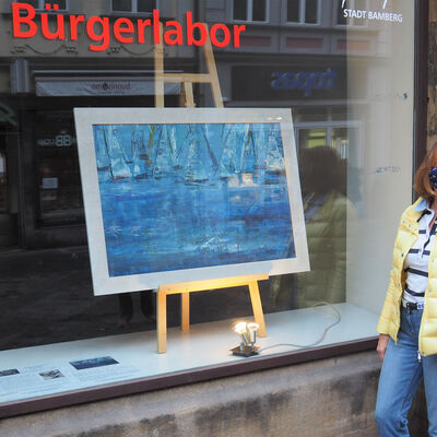 Bild vergrößern: Foto: Nadja Rakowski steht vor dem Bürgerlabor, in dem ihr Bild »Dynamik in Blau« ausgestellt ist.