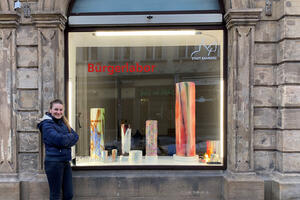 Bild vergrößern: Bild: Stefanie Brehm vor dem Kunstfenster, in dem bunte Keramiksäulen ausgestellt sind.