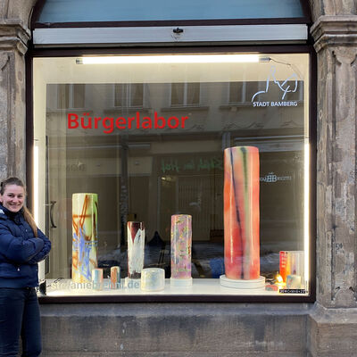 Bild vergrößern: Bild: Stefanie Brehm vor dem Kunstfenster, in dem bunte Keramiksäulen ausgestellt sind.