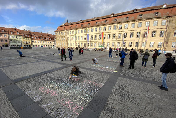 Bild vergrößern: Schülerinnen schreiben die Namen der Deportierten mit bunter Kreide auf den Maxplatz.