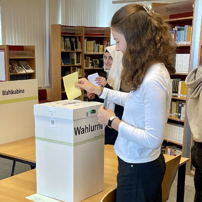 Bild vergrößern: Eine Schülerin beim Einwurf ihres Stimmzettels in die versiegelte Wahlurne.